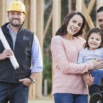 An Hispanic family with a cute little 3 year old daughter, at the construction site where their new home is being built. They are smiling and looking at the camera, the couple holding their child between them, excited that they will soon be home owners. A building contractor or construction worker is standing next to them.